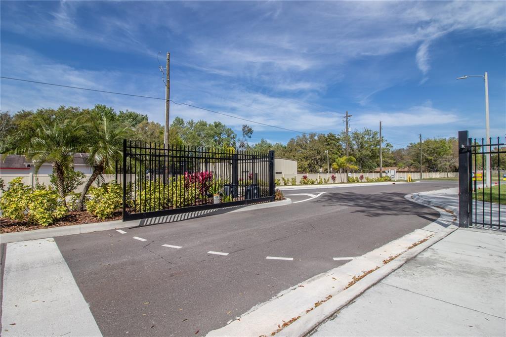 A black metal gate stands at the entrance of a paved driveway under a blue sky — 3333 PLEASANT WILLOW COURT, BRANDON, FL