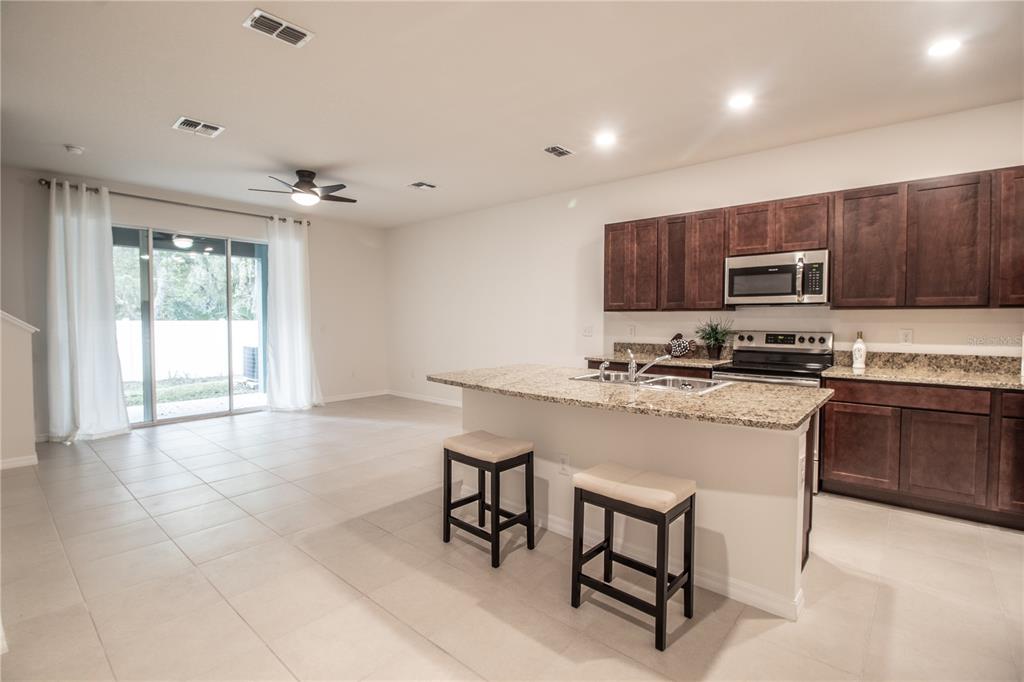 A kitchen with dark wood cabinets, granite countertops, and an island with two bar stools — 3333 PLEASANT WILLOW COURT, BRANDON, FL