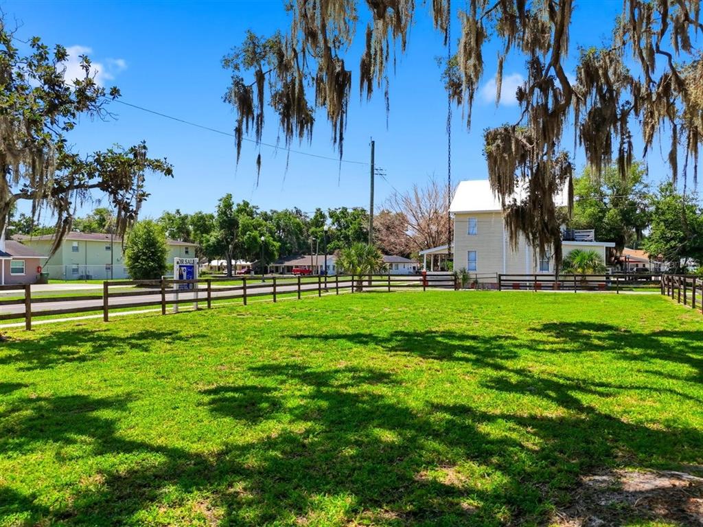 A fenced, grassy lot with mature trees and a yellow house in the background — 702 AVENUE A, WINTER HAVEN, FL