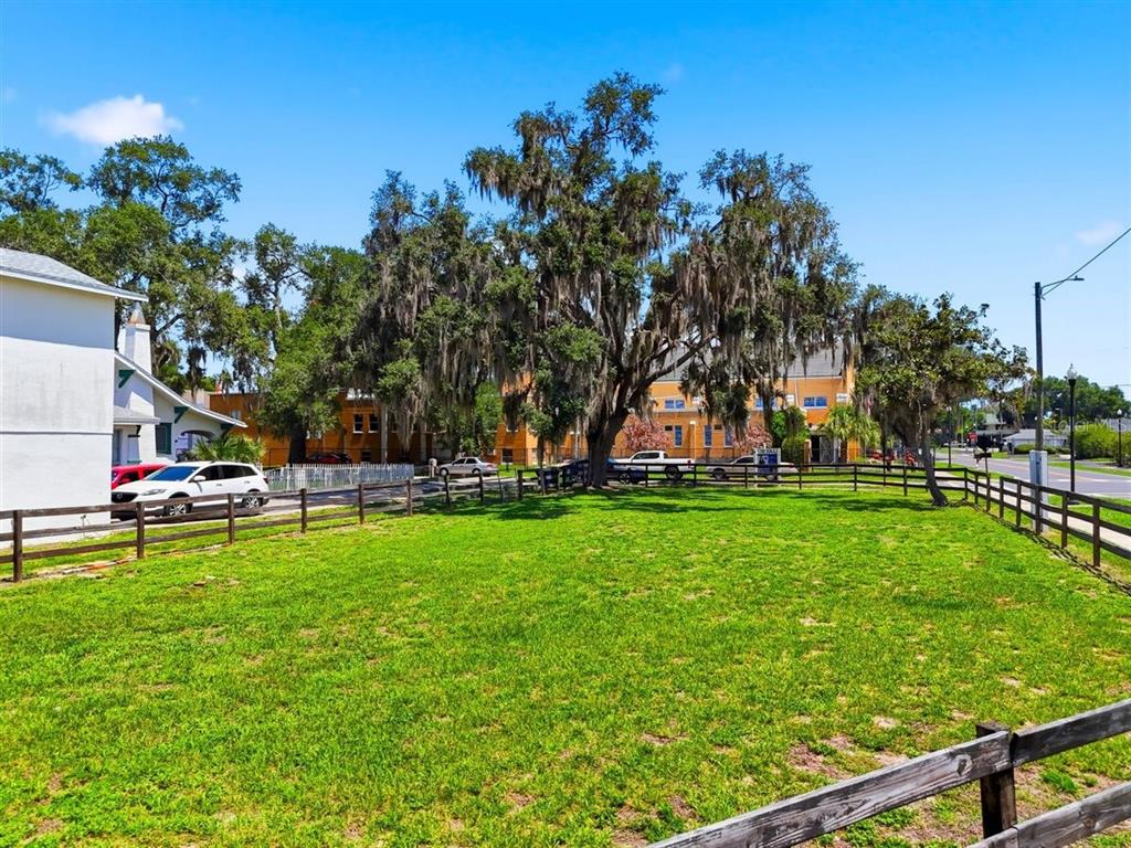 A grassy lot is enclosed by a wooden fence with large trees in the background — 702 AVENUE A, WINTER HAVEN, FL