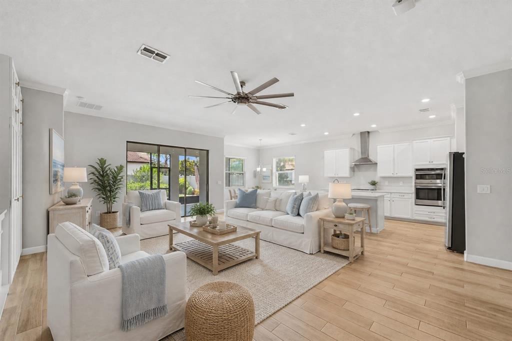 An open-concept living room and kitchen featuring light wood floors, white cabinetry, and neutral furniture — 16920 SCUBA CREST STREET, WIMAUMA, FL