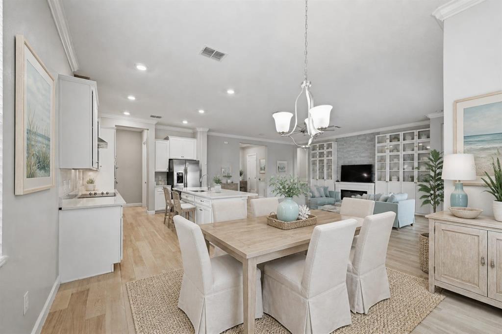 An open-concept kitchen and dining area featuring white cabinetry, light wood floors, and a chandelier — 16920 SCUBA CREST STREET, WIMAUMA, FL