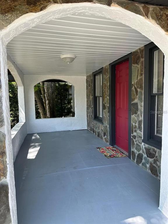A covered porch features a red front door, stone walls, and a gray painted floor — 221 N JULIA AVENUE, DELAND, FL