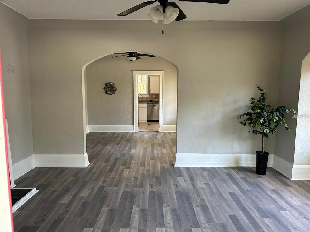 A living room with gray wood-look flooring leads through an arched doorway to a kitchen — 221 N JULIA AVENUE, DELAND, FL