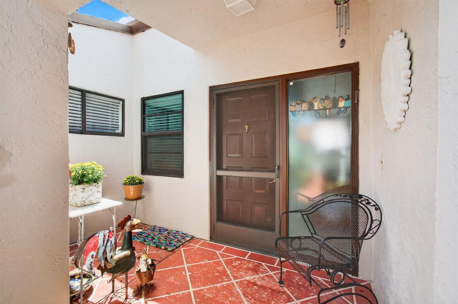 An outdoor entryway features a red tiled floor, a brown door, and a metal chair — 6248 Kings Gate Circle, Delray Beach FL 33484, DELRAY BEACH, FL