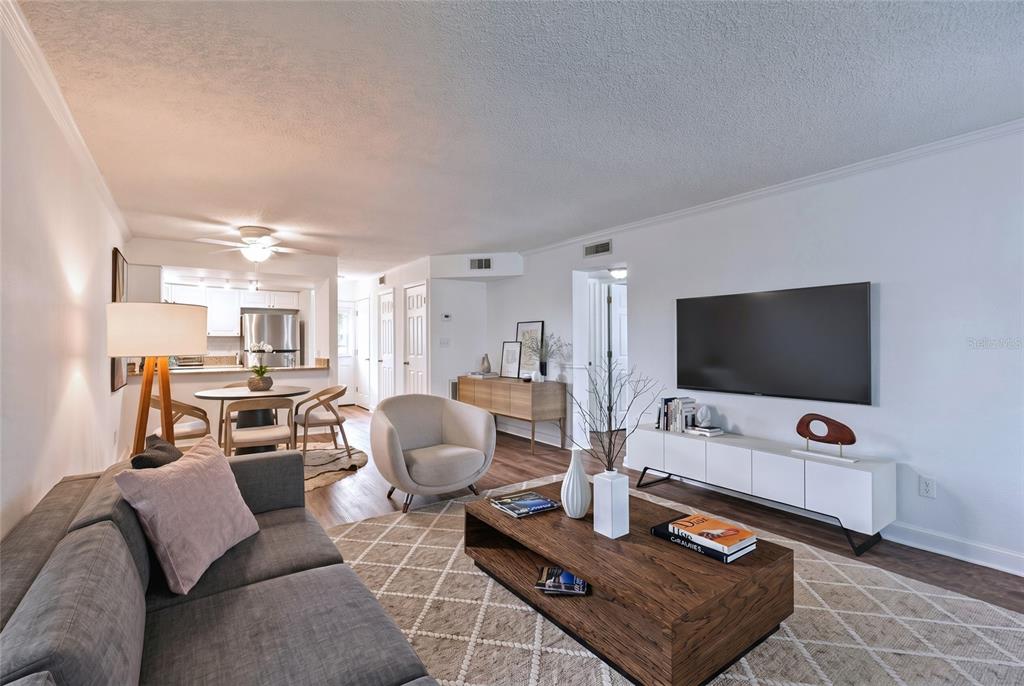 An open-concept living area features wood-look flooring, white walls, and a view into the kitchen — 4813 MCELROY UNIT D108, TAMPA, FL