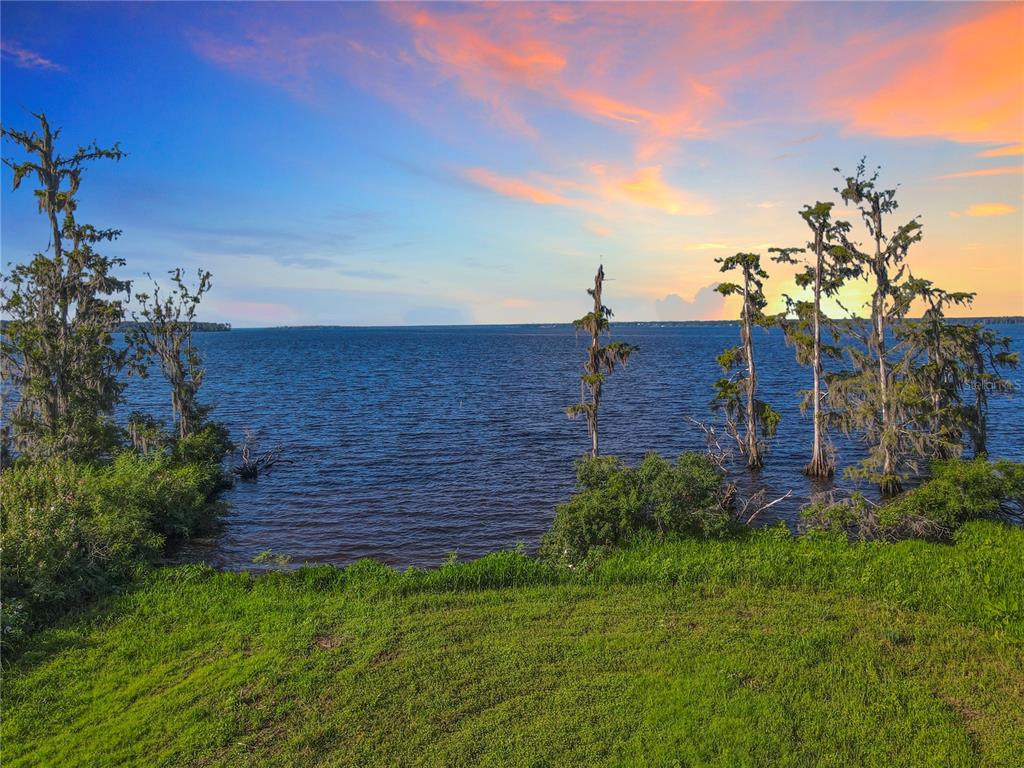 A grassy lawn overlooks a lake with cypress trees growing in the water at sunset — 14453 ANDALUSIA TRAIL, BUNNELL, FL