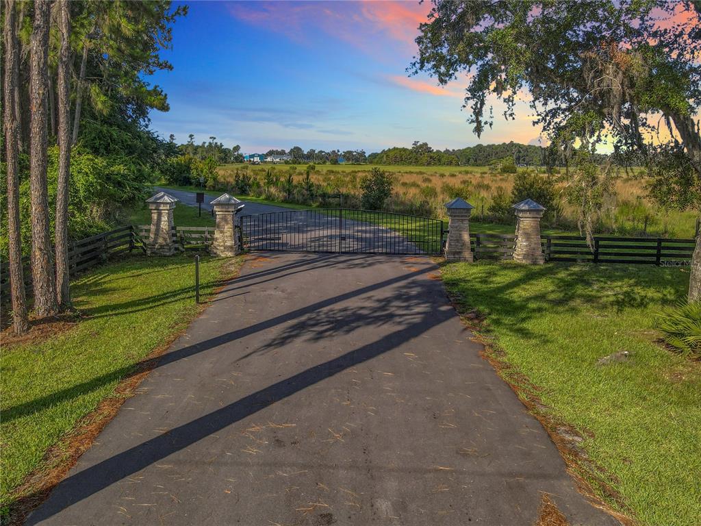 A paved driveway leads to a gated entrance with stone pillars and a fenced perimeter — 14453 ANDALUSIA TRAIL, BUNNELL, FL
