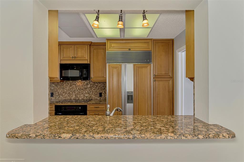 A kitchen view features granite countertops, wood cabinetry, a built-in refrigerator, and a breakfast bar — 4438 LONG COMMON LANE UNIT 52, SARASOTA, FL
