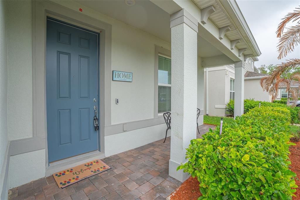 A blue front door with a welcome mat sits on a paved porch with columns — 4120 RAINFALL PLACE, SANFORD, FL