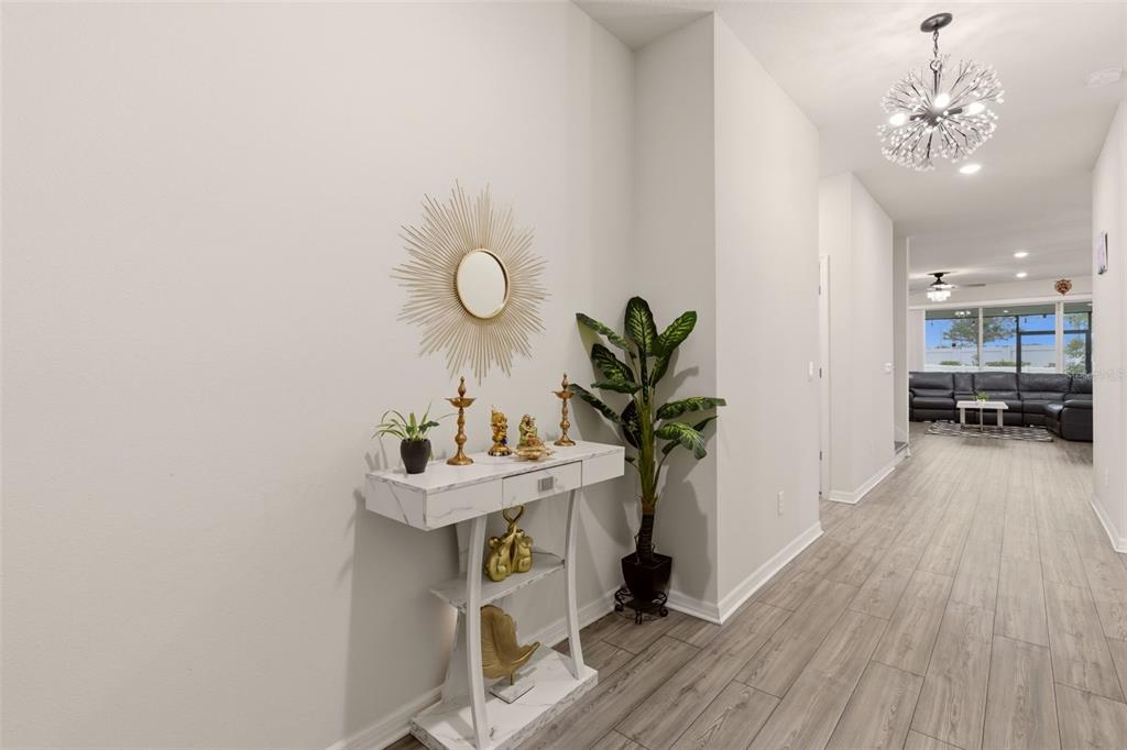 A white marble console table sits in a hallway with a sunburst mirror and plant — 4120 RAINFALL PLACE, SANFORD, FL