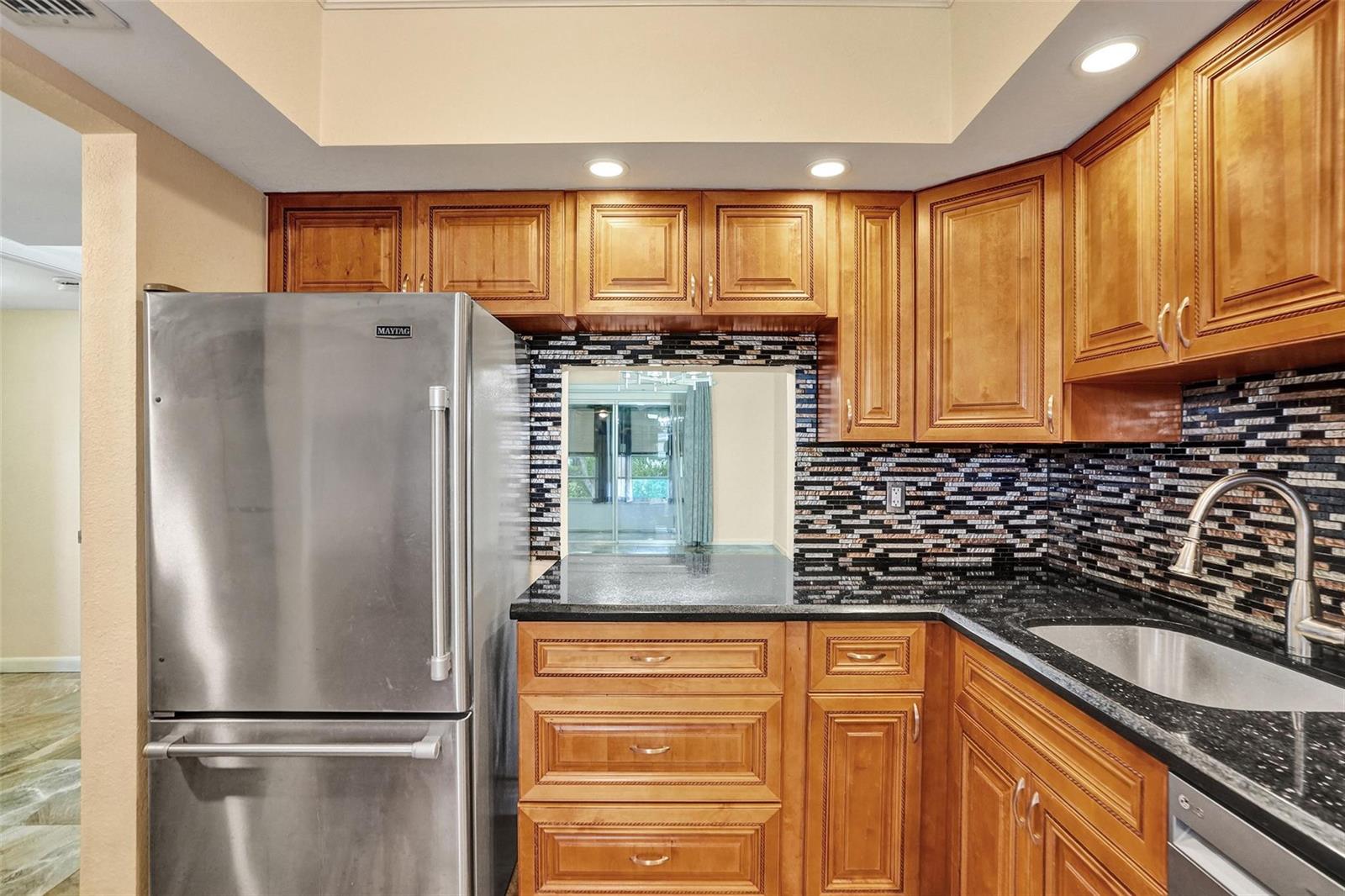 A kitchen with wood cabinets, black granite countertops, a stainless steel refrigerator, and mosaic backsplash — 651 NW 80th Terrace # 207, Margate FL 33063, MARGATE, FL