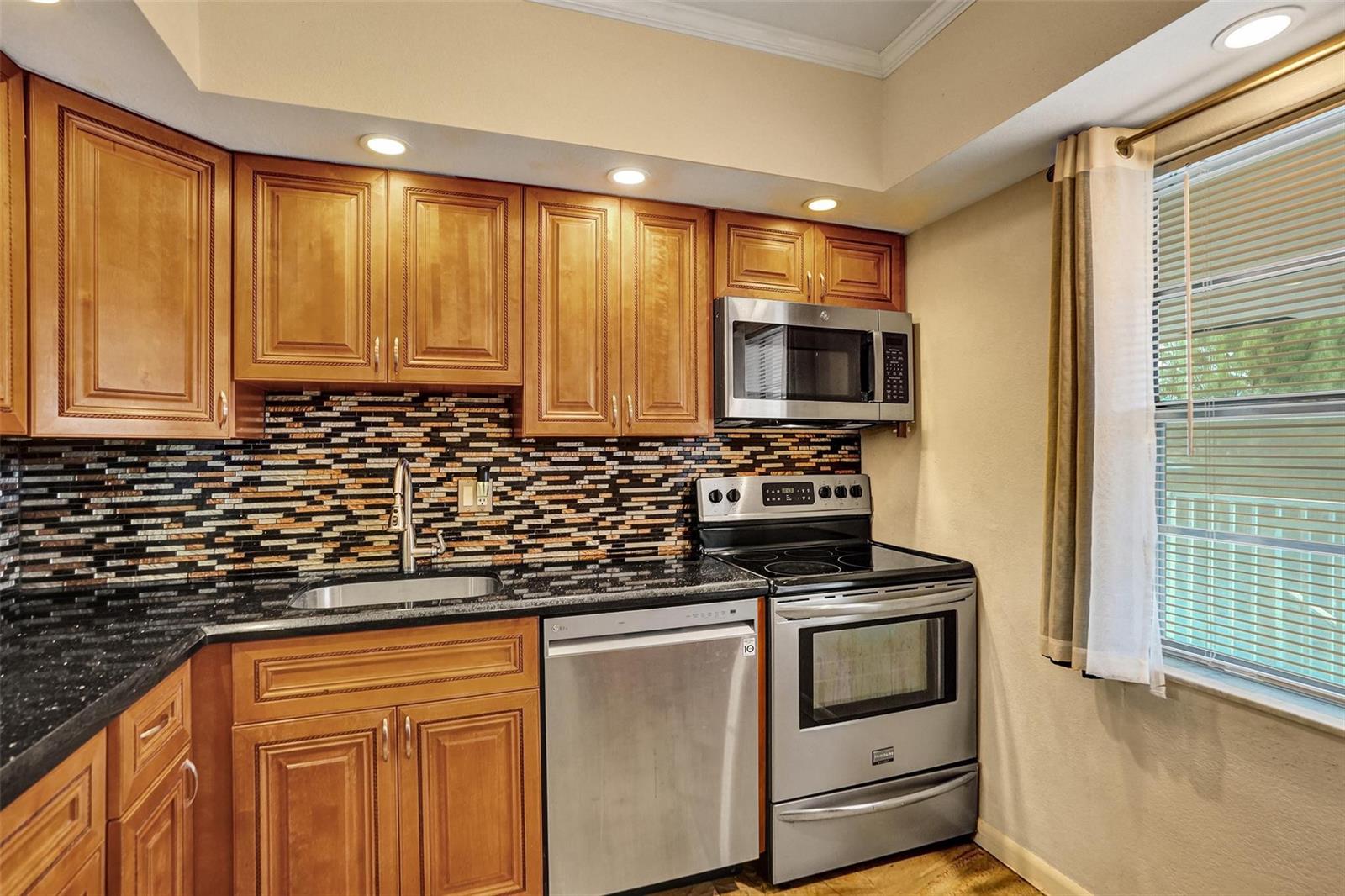 A kitchen with wood cabinets, stainless steel appliances, black countertops, and a mosaic tile backsplash — 651 NW 80th Terrace # 207, Margate FL 33063, MARGATE, FL
