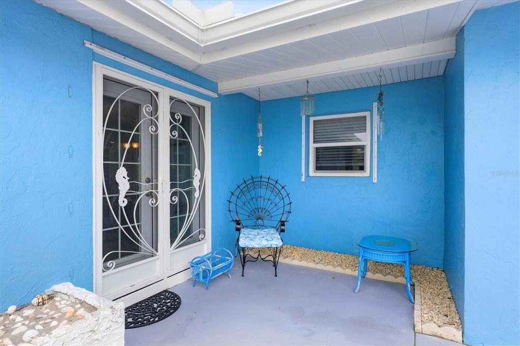 A bright blue covered patio features a decorative metal chair, small table, and glass doors — 12 GOLFVIEW COURT, ROTONDA WEST, FL
