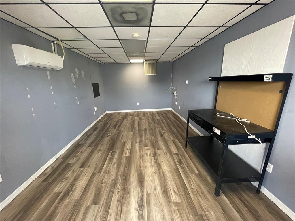 A room with gray walls, wood-look flooring, a drop ceiling, and a black workbench — 4849 SE 110TH STREET UNIT 61, BELLEVIEW, FL