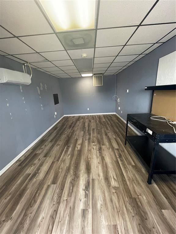 An empty room features gray walls, wood-look flooring, a drop ceiling, and a black workbench — 4849 SE 110TH STREET UNIT 61, BELLEVIEW, FL