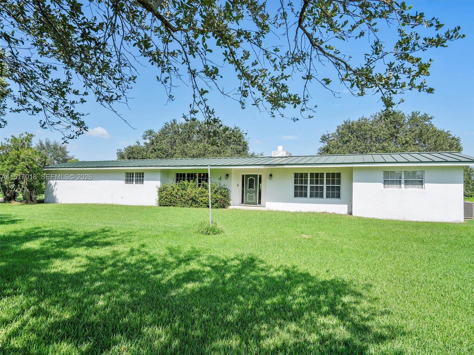 A single-story white house with a green metal roof sits on a large grassy lawn — 5901 SW 160th Ave, Southwest Ranches FL 33331, SOUTHWEST RANCHES, FL