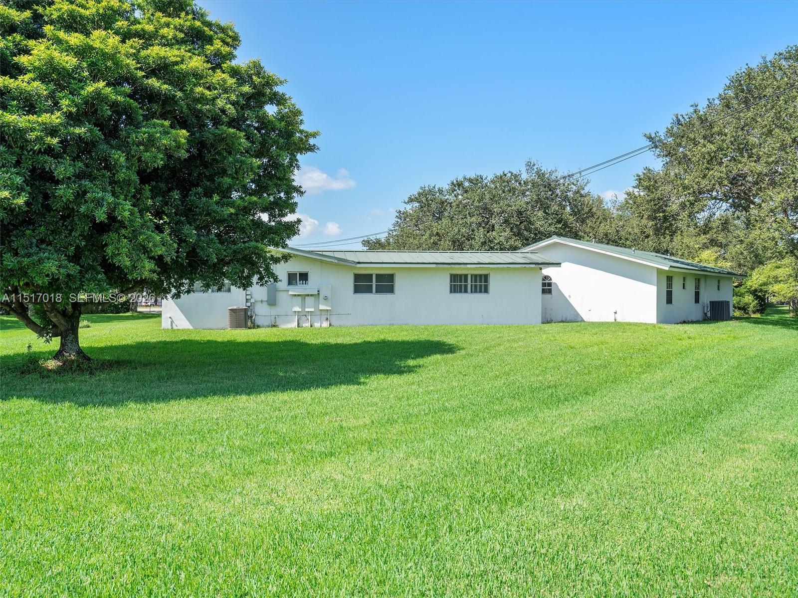 A white, single-story house with a green metal roof sits on a large grassy lawn — 5901 SW 160th Ave, Southwest Ranches FL 33331, SOUTHWEST RANCHES, FL