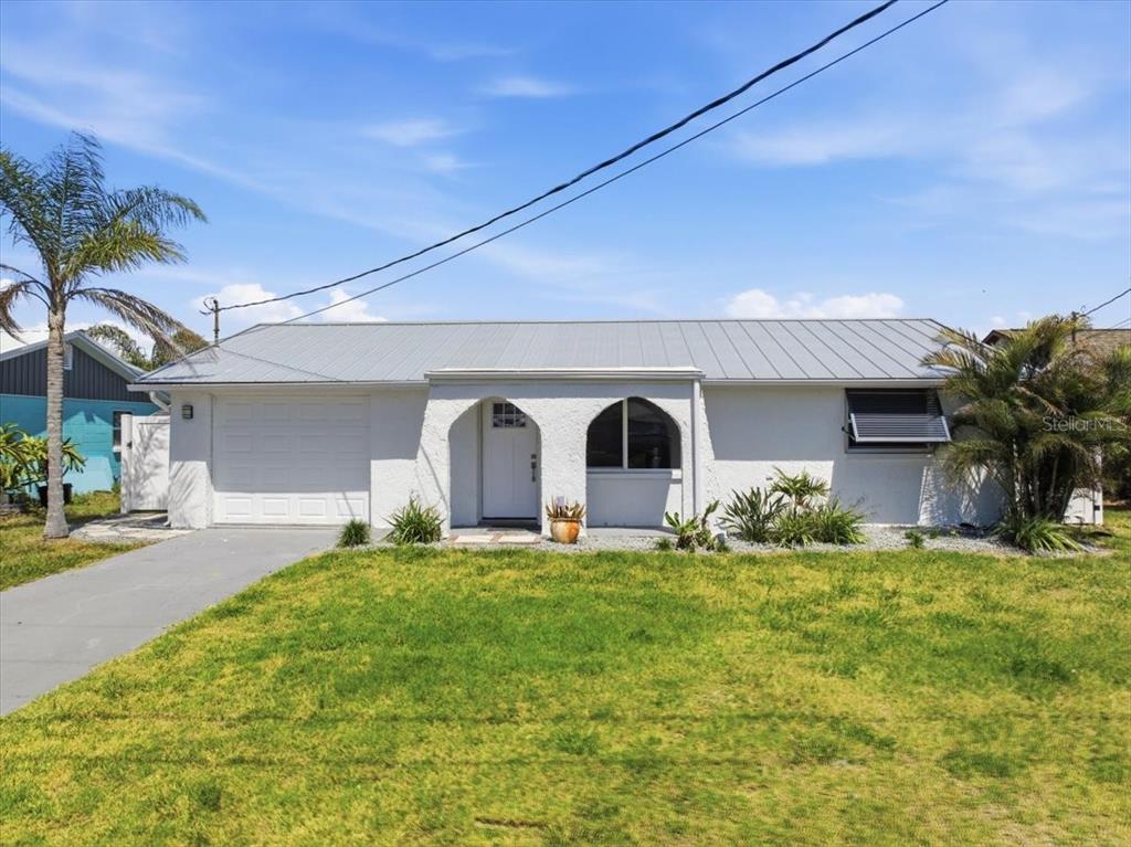 A single-story house with a white stucco exterior, metal roof, and an attached garage — 13902 BARNARD AVENUE, HUDSON, FL