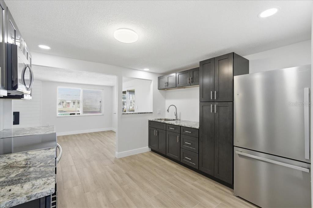 A kitchen features dark cabinetry, stainless steel appliances, granite countertops, and light wood-look flooring — 13902 BARNARD AVENUE, HUDSON, FL