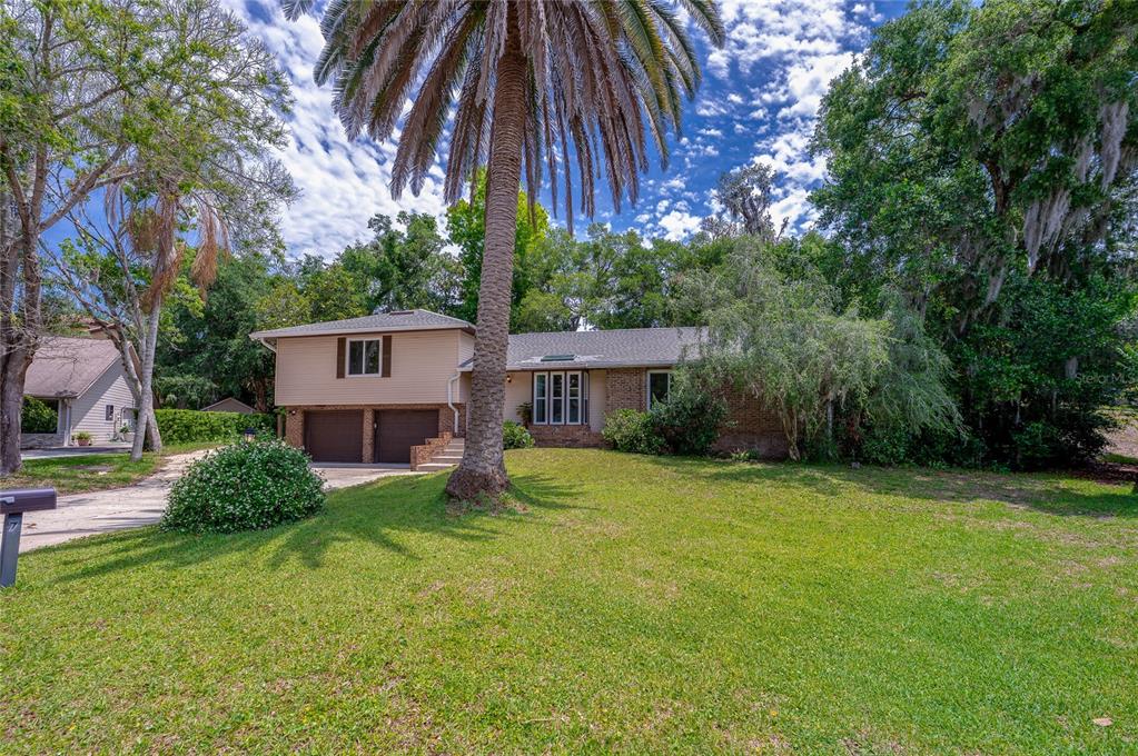 A split-level house with a two-car garage, a large palm tree, and a grassy yard — 7 WATERFRONT COURT, ORMOND BEACH, FL