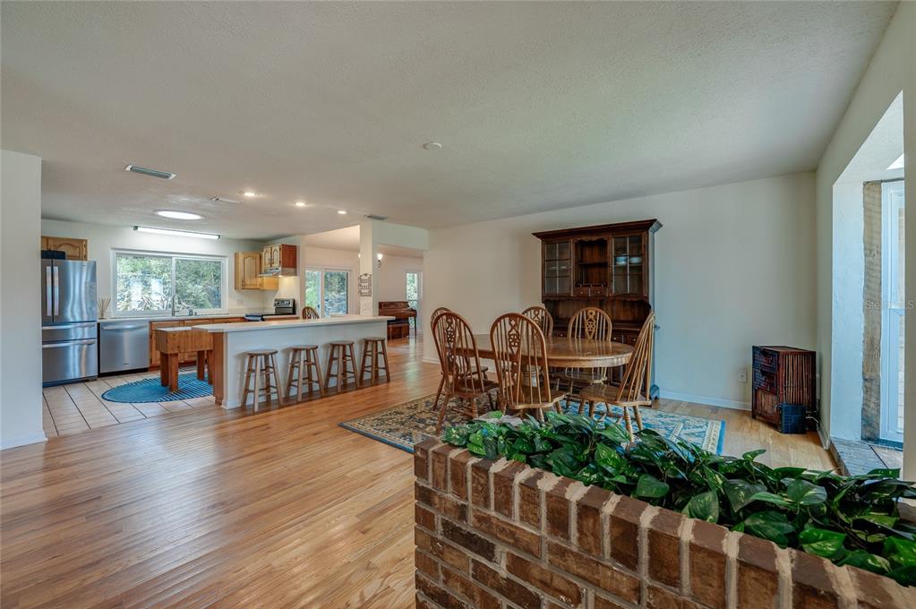 An open-concept kitchen and dining area features hardwood floors, a brick planter, and wooden furniture — 7 WATERFRONT COURT, ORMOND BEACH, FL