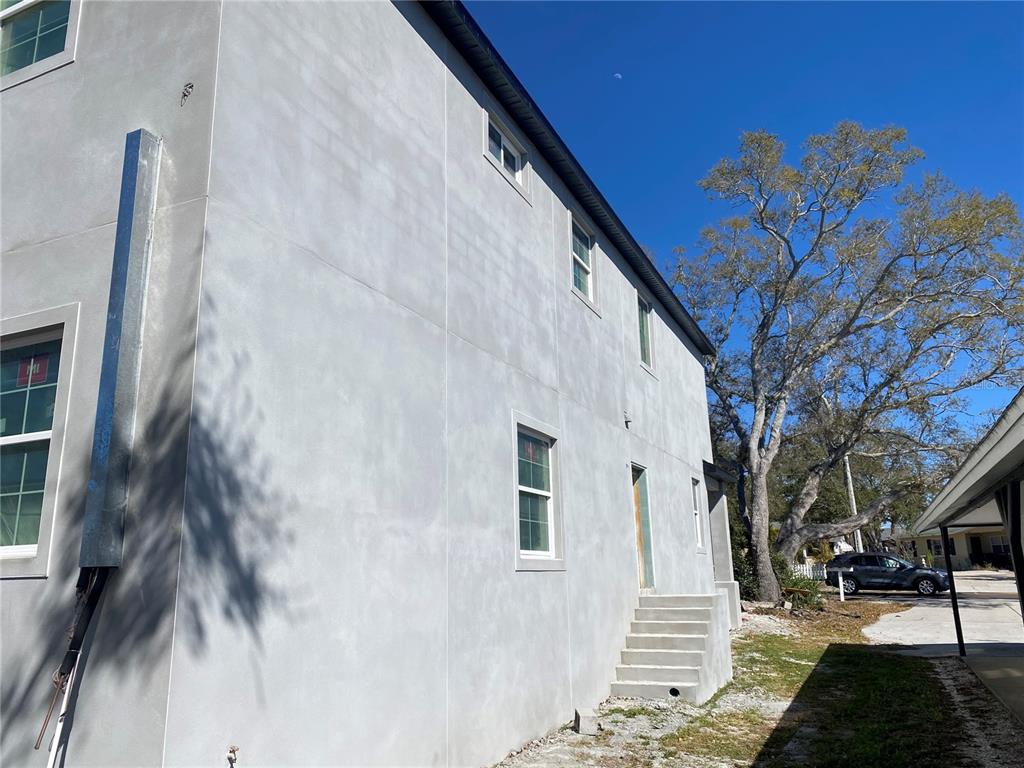 The exterior of a two-story house features gray stucco walls and a set of concrete stairs — 1040 BASS BOULEVARD, DUNEDIN, FL
