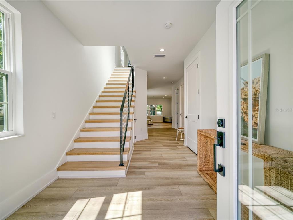 A bright entryway features light wood flooring, a staircase with metal railings, and white walls — 1040 BASS BOULEVARD, DUNEDIN, FL