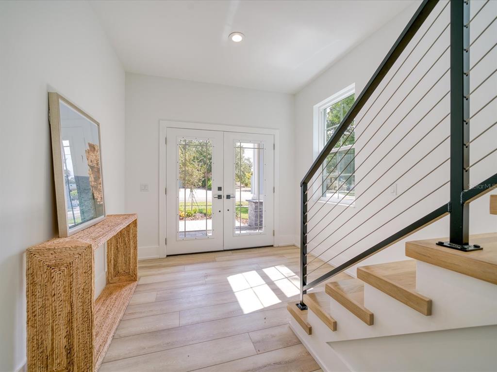 A bright entryway features light wood flooring, a woven console table, and a modern staircase — 1040 BASS BOULEVARD, DUNEDIN, FL