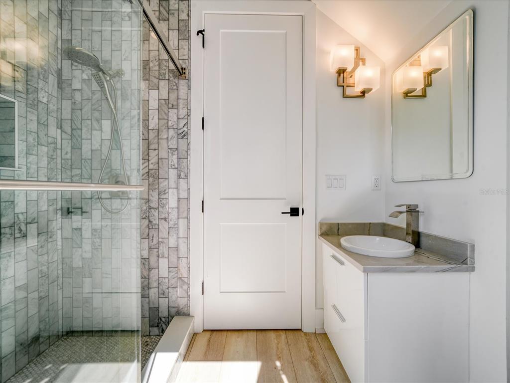 A bathroom features a glass-enclosed marble shower, a white vanity, and light wood-look flooring — 1040 BASS BOULEVARD, DUNEDIN, FL