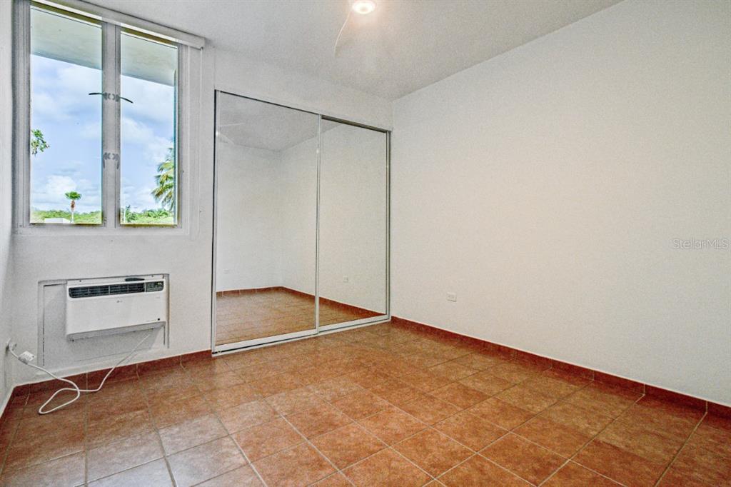 A bedroom features tiled floors, a mirrored closet, and a window air conditioning unit — 693 NCV UNIT 324, VEGA ALTA, PR