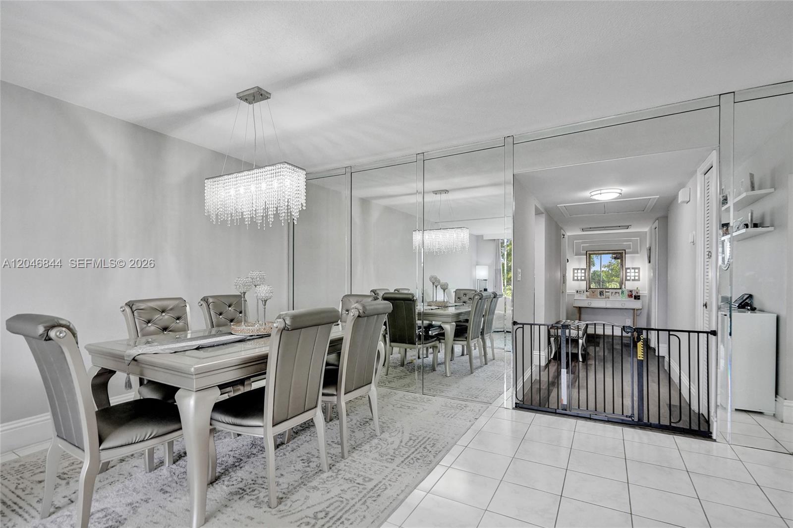 A dining room features a crystal chandelier, mirrored walls, and a black metal safety gate — 2651 S Course Dr # 410, Pompano Beach FL 33069, POMPANO BEACH, FL