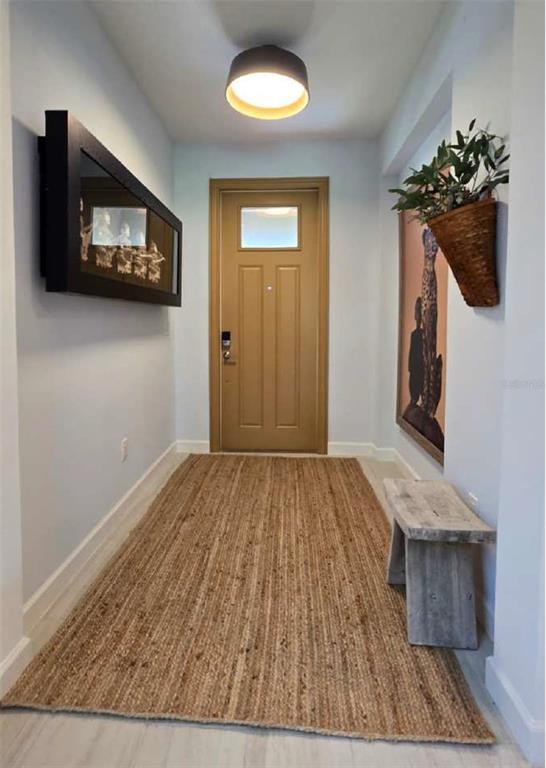 A hallway features a tan door, a jute rug, a wooden bench, and wall art — 10583 TUPPER CAY DRIVE, SAN ANTONIO, FL