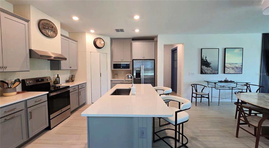 A modern kitchen features gray cabinetry, a large white quartz island, and stainless steel appliances — 10583 TUPPER CAY DRIVE, SAN ANTONIO, FL