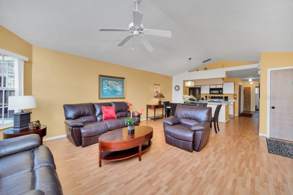 A living room with light wood flooring, yellow walls, and brown leather furniture — 3139 BRITANNIA BOULEVARD UNIT C, KISSIMMEE, FL