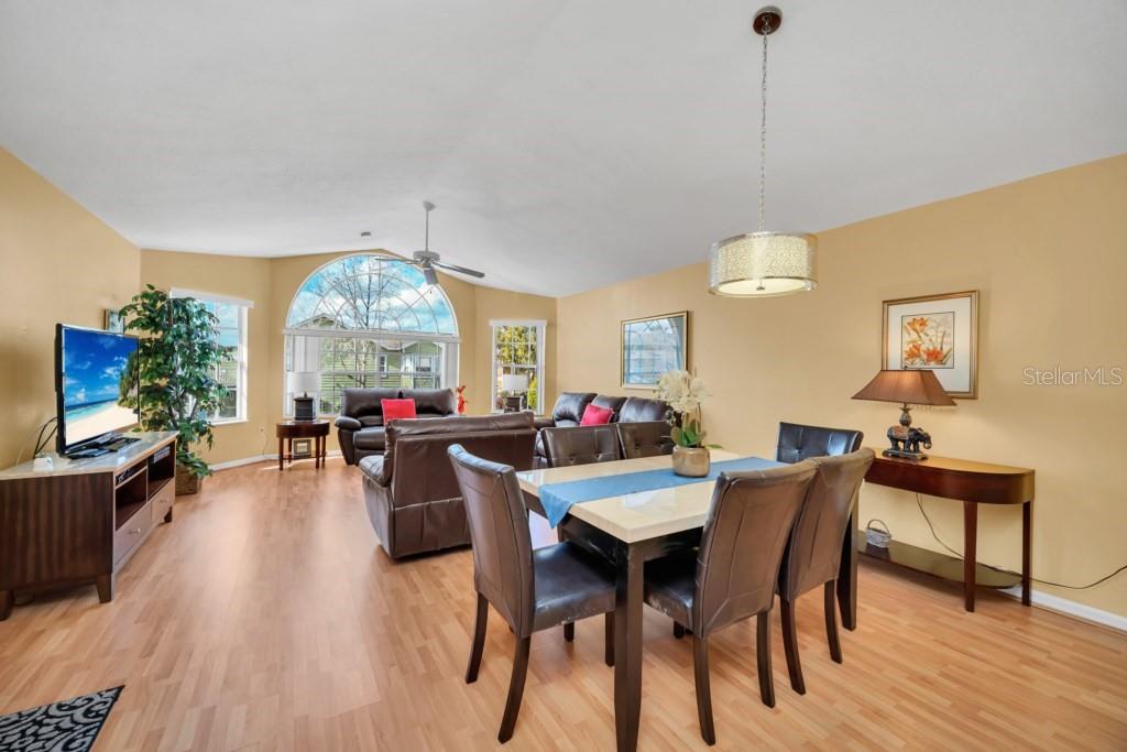 A living and dining room with light wood floors, vaulted ceilings, and a large arched window — 3139 BRITANNIA BOULEVARD UNIT C, KISSIMMEE, FL