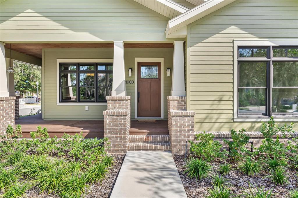 A front porch with a wooden door, brick columns, and light green horizontal siding — 1000 S 9TH STREET, LEESBURG, FL