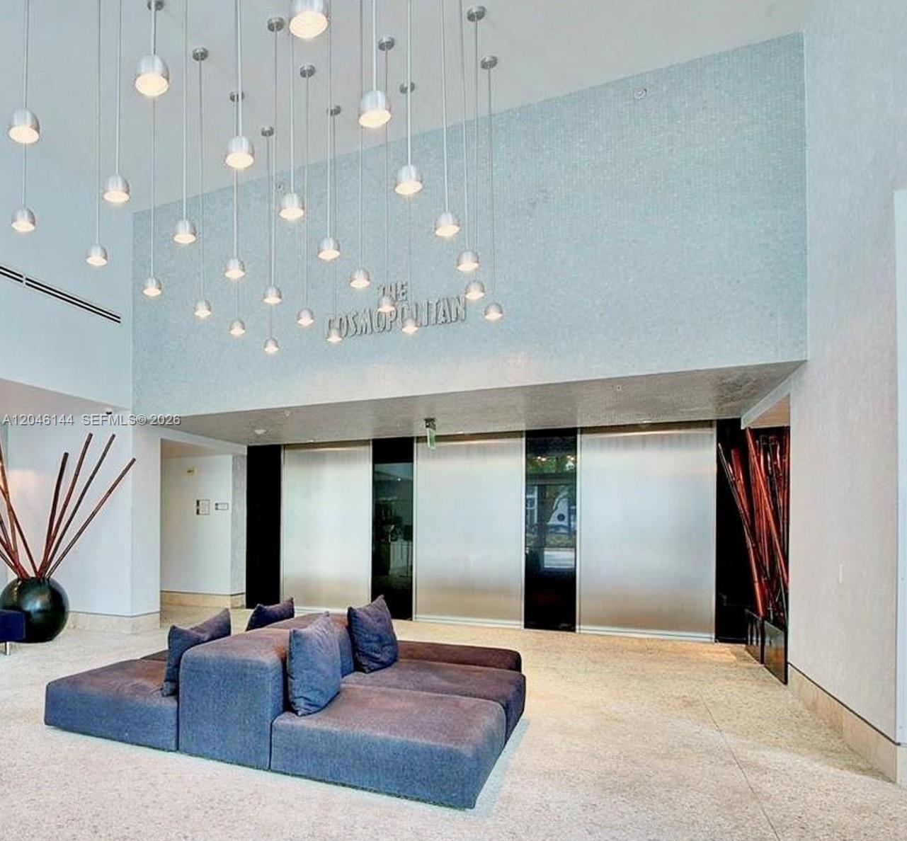 A modern building lobby features a large gray sectional sofa, hanging pendant lights, and elevators — 110 Washington Ave # 1506, Miami Beach FL 33139, MIAMI BEACH, FL