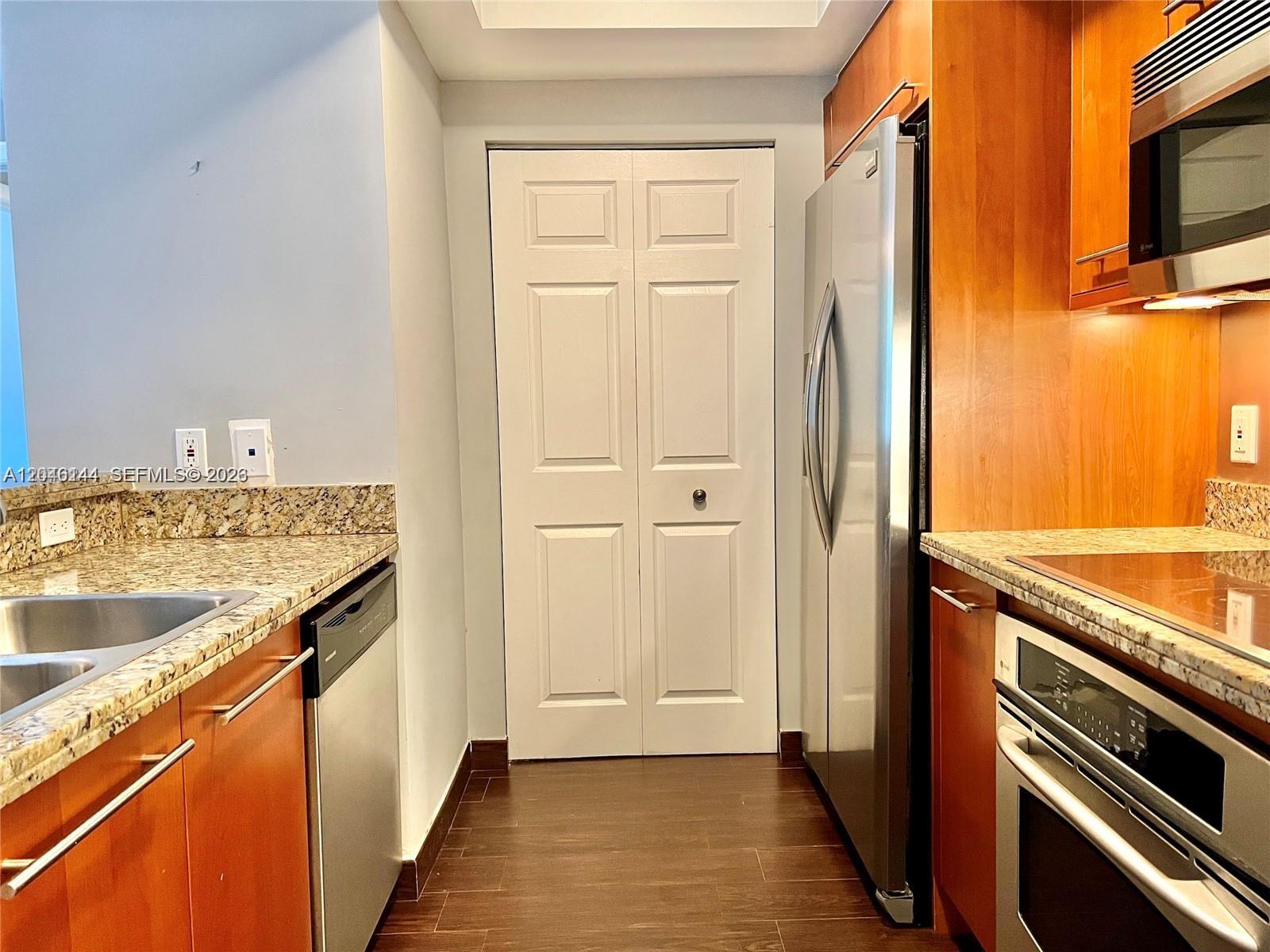 A kitchen features stainless steel appliances, wood cabinets, granite countertops, and a white bi-fold door — 110 Washington Ave # 1506, Miami Beach FL 33139, MIAMI BEACH, FL