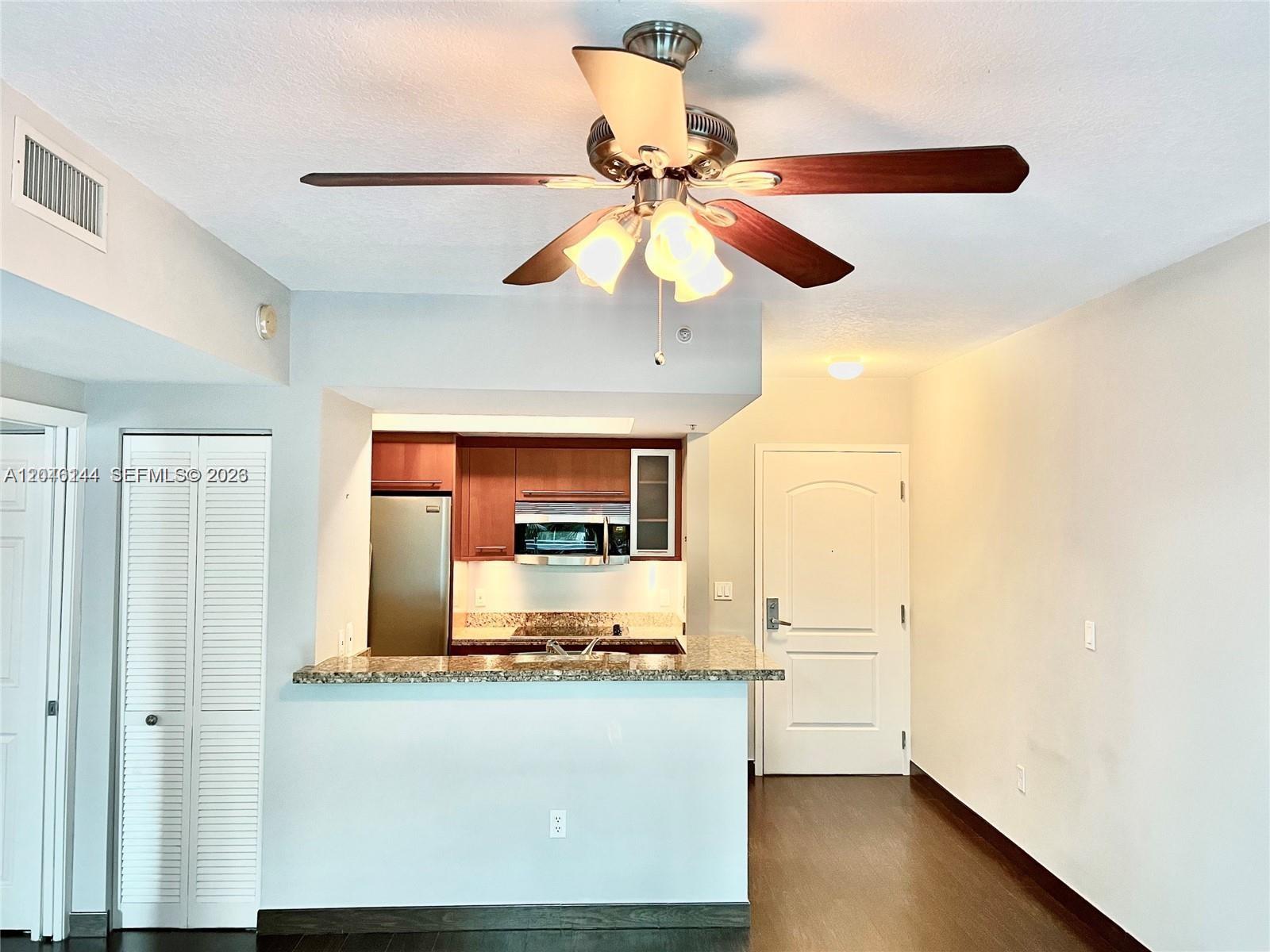 A kitchen with wood cabinets and granite counters opens to a living area with flooring — 110 Washington Ave # 1506, Miami Beach FL 33139, MIAMI BEACH, FL