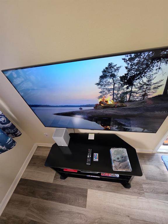 A wall-mounted television sits above a black media console in a room with wood-look flooring — 2751 N POINCIANA BOULEVARD UNIT 30, KISSIMMEE, FL