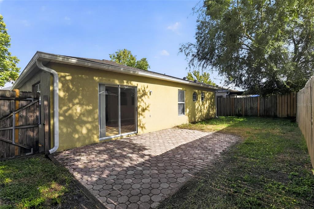 A yellow house exterior features a paved patio, sliding glass doors, and a wooden fence — 1080 AMANDA KAY CIRCLE, SANFORD, FL
