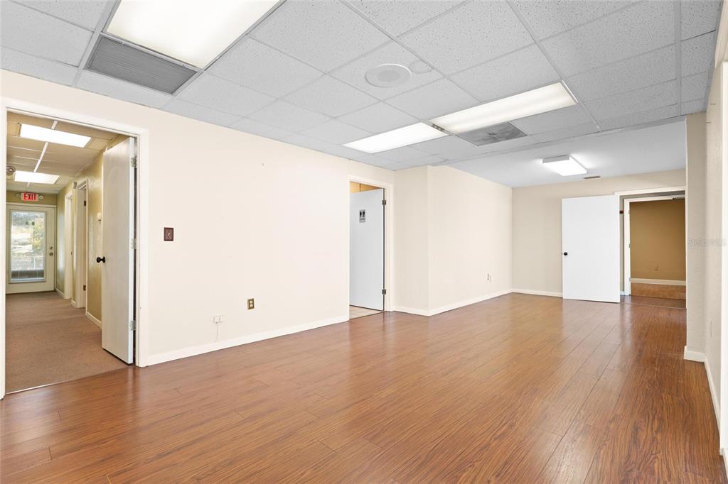 An empty office space features wood-look flooring, a drop ceiling with fluorescent lights, and multiple doorways — 1200 S PINELLAS AVENUE, TARPON SPRINGS, FL