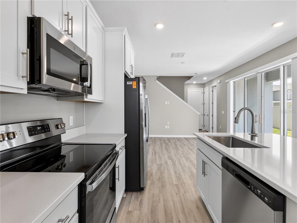A modern kitchen features white cabinets, stainless steel appliances, and a quartz-topped island — 1465 AXEL GRAESON AVENUE, KISSIMMEE, FL