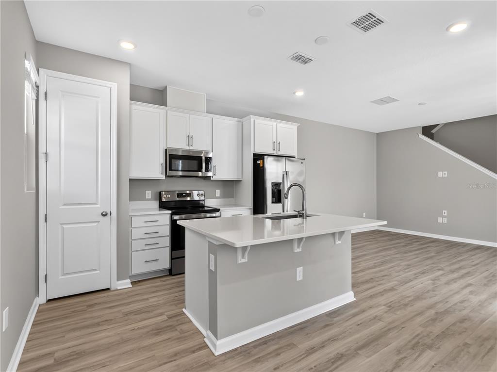 A modern kitchen features white cabinets, stainless steel appliances, a quartz island, and wood flooring — 1465 AXEL GRAESON AVENUE, KISSIMMEE, FL