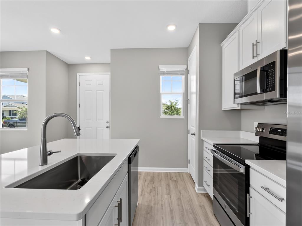 A modern kitchen features white cabinets, a quartz-topped island with a sink, and stainless appliances — 1465 AXEL GRAESON AVENUE, KISSIMMEE, FL