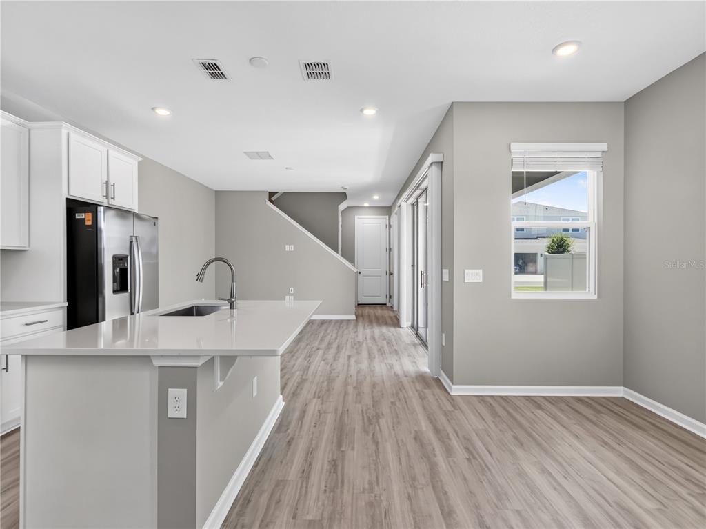A modern kitchen features a white island with a sink, stainless steel appliances, and wood-look flooring — 1465 AXEL GRAESON AVENUE, KISSIMMEE, FL