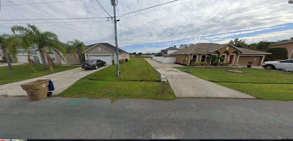 A vacant grassy lot sits between two suburban houses with concrete driveways — 523 ELBRIDGE PLACE, POINCIANA, FL