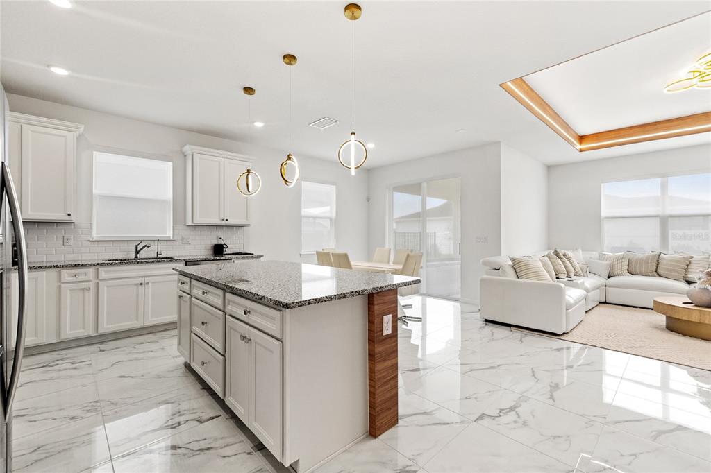 A modern open-concept kitchen and living area with white cabinetry, granite countertops, and marble flooring — 6976 ROSY SKY AVENUE, ORLANDO, FL