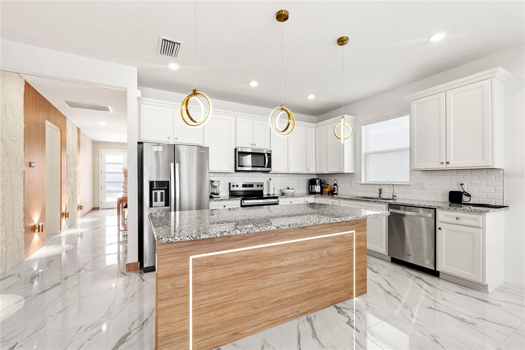 A modern kitchen features white cabinets, granite countertops, a wood-paneled island, and marble-look tile flooring — 6976 ROSY SKY AVENUE, ORLANDO, FL